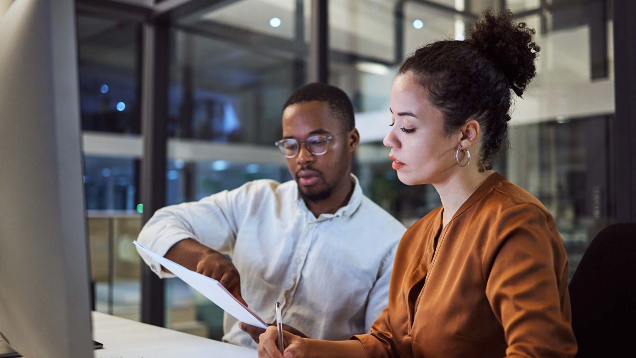 Coworkers discuss a document in front of a computer