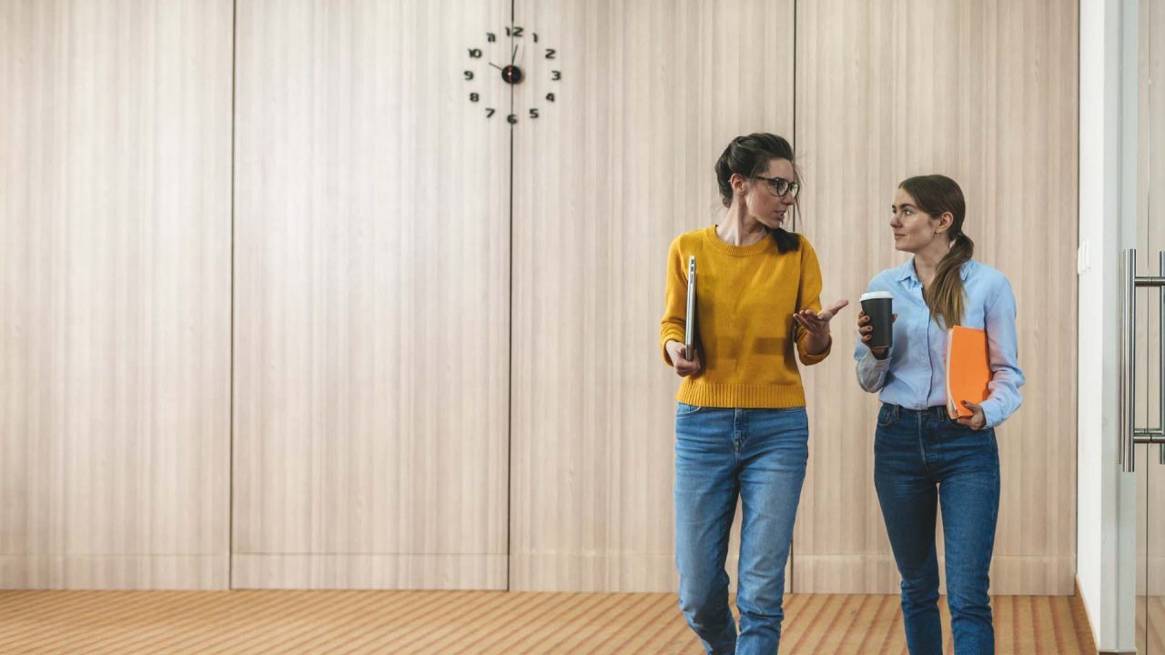 two women colleagues having a work conversation in a modern hallway