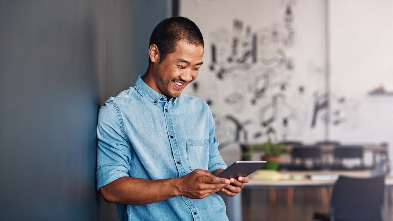 A smiling man is typing on a tablet computer
