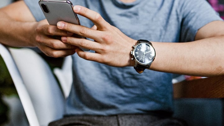 Et nærbillede af en persons hænder, der holder og bruger en sølvfarvet smartphone.