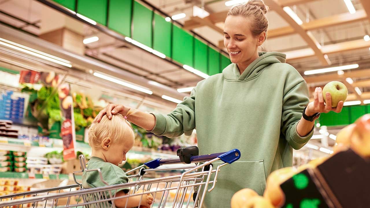 woman in grocery store holding apple with child in cart