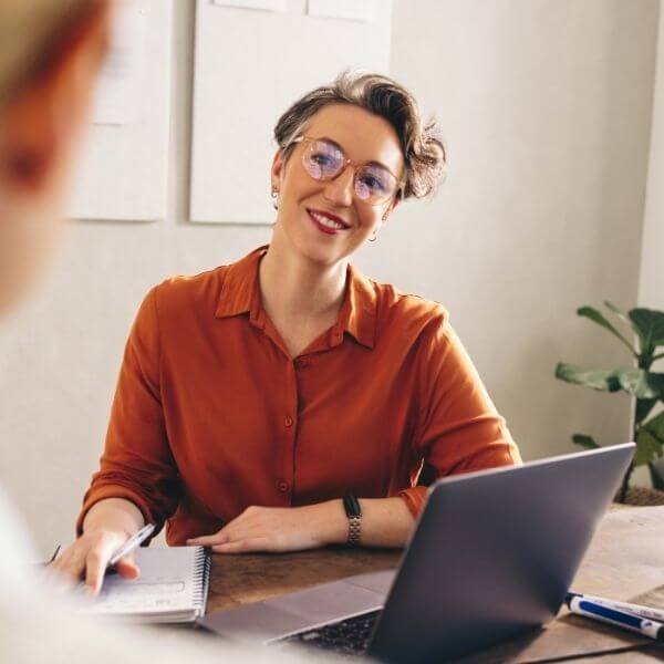 business woman in orange shirt at desk meeting with colleague