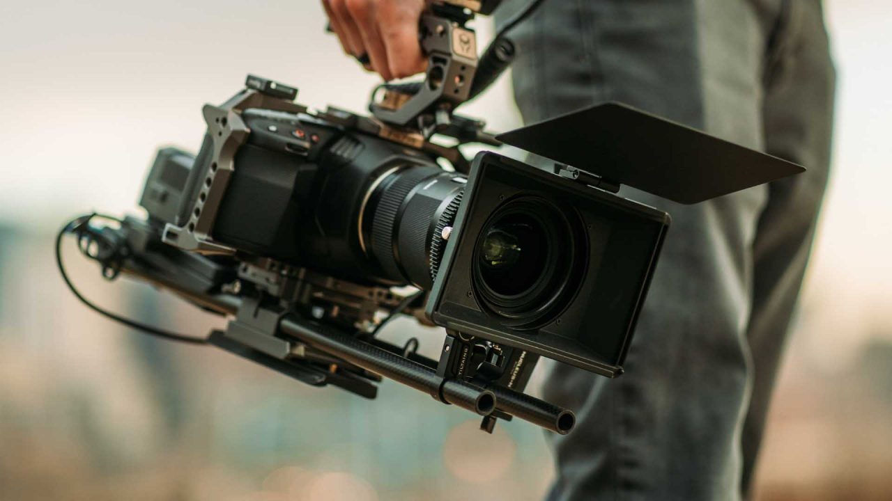 A detailed view of a high-end video camera with professional accessories, held by someone ready to film.