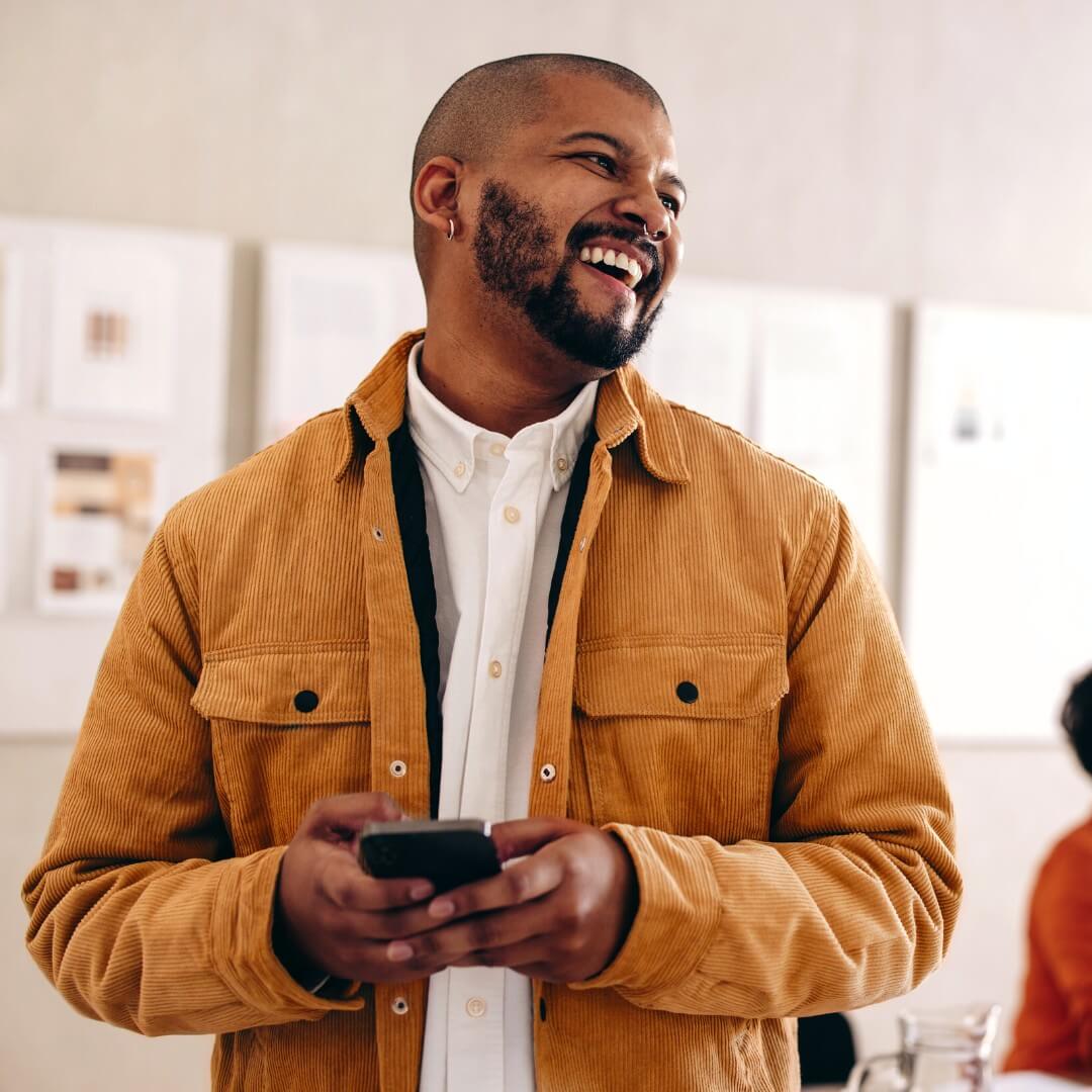 man with yellow jacket smiling and holding mobile phone in office
