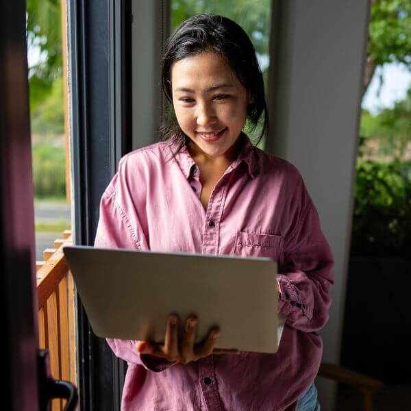 woman in pink shirt standing while working on laptop from home